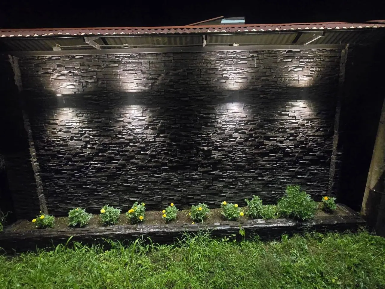 Tapia de piedra negra iluminada con luces de pared