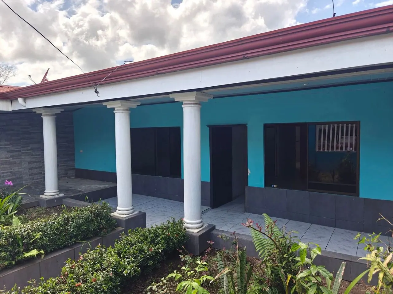 Casa turquesa con corredor de columnas blancas y jardín al frente