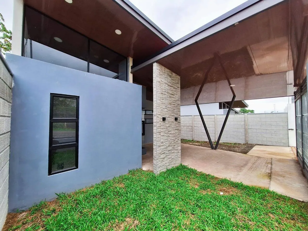 Costado de la casa con zacate y ventanas angostas