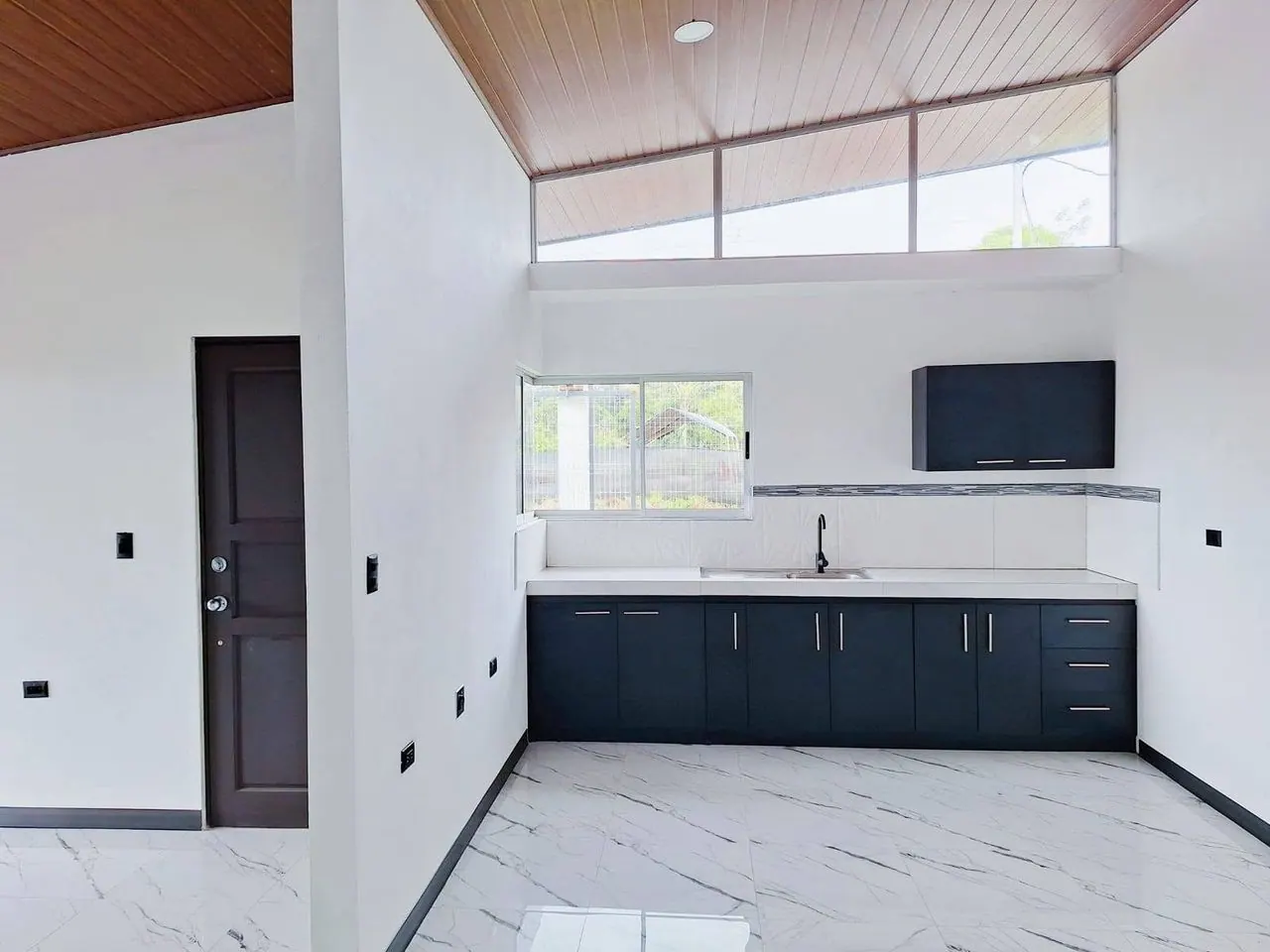 Cocina con muebles negros bajo ventanas altas