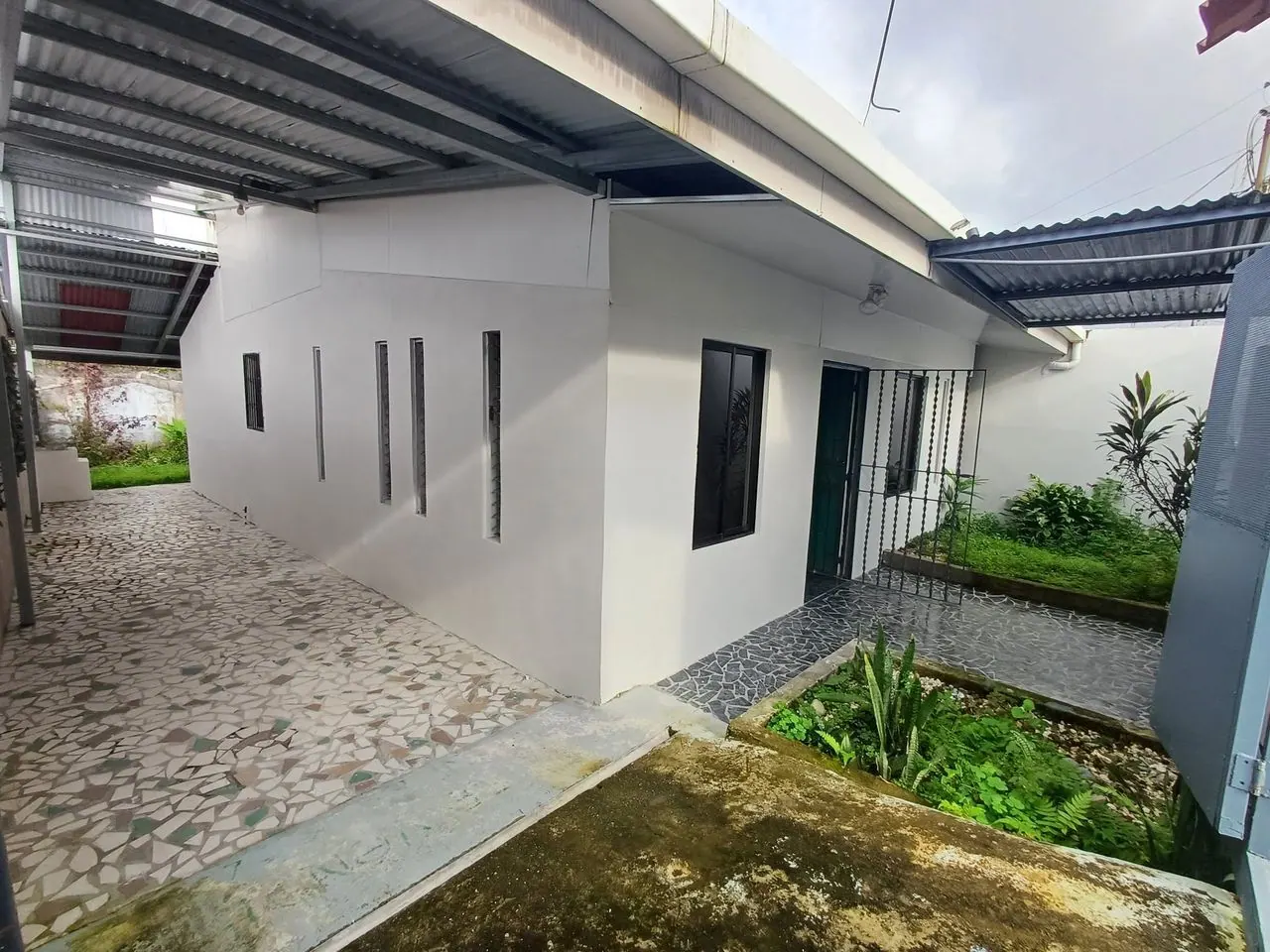 Casa blanca de ventanas angostas con jardín y camino de piedra