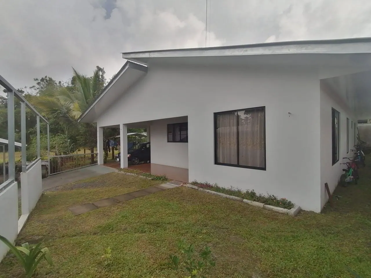 Casa blanca de una planta con cochera y zacate al frente